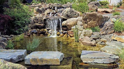 The Garden Artist created a waterfall that spills into a fishpond, which is flanked by a walkway of stones that appear to float above the water.