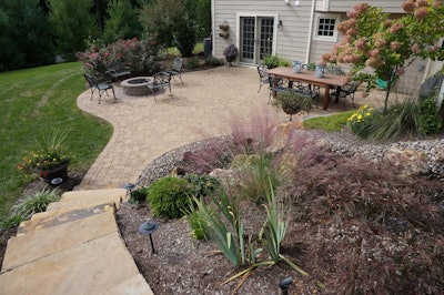 At the end of the curved stairs made of stone, lies a patio built of pavers also featuring a firepit.