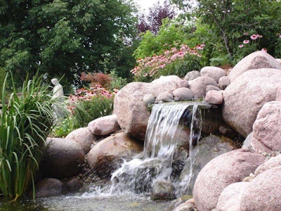 Watched over by a saint, this waterfall and garden features plantings both submerged in and surrounding the pond. RGMI does plenty of heavy lifting in its construction, installation and snow-removal operations but also has opportunities, as in this job, to show off its eye for design. Photo: Reinhart Grounds Maintenance