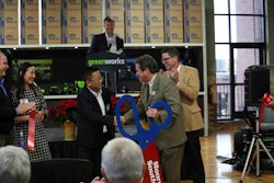 Greenworks Tools CEO and owner, Yin Chen, receives congratulations from Chairman of the Mooresville/South Iredell Chamber of Commerce, Kirk Ballard, as Mooresville Mayor Miles Atkins (right) and Greenworks President, Chris Allen (at podium) look on during Greenworks Tools opening of its new headquarters in Mooresville, North Carolina.