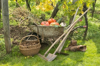 fall scenery with a wheelbarrow full of pumpkins, gardening tools, basket full of nuts, and worker boots