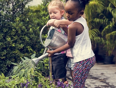 two children using a watering can to water the flowers in the garden