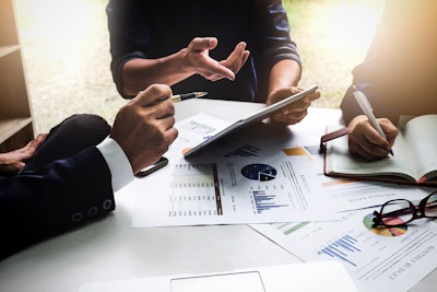 team of three collaborating at a desk with tablet and pen and paper