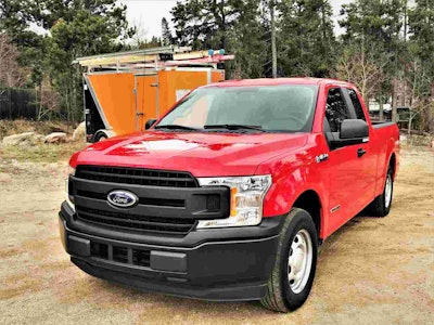 Red Ford F-150 Diesel Pick up truck parked on a dirt construction site pulling an orange trailer with ladders strapped onto the top of the trailer