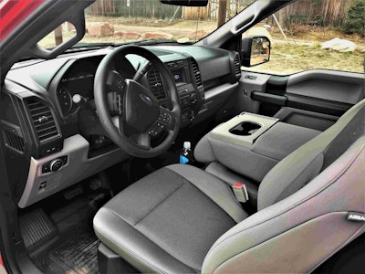 Grey front seat interior of Ford F-150 Diesel Truck, black steering wheel, arm wrest with cup holders,