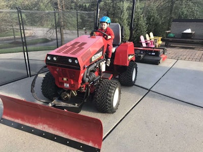 photo of young child in red sweats with a blue bicycle helmet behind the wheel of a big red tractor