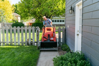 Man using Kubota scl1000 mini skid steer in backyard