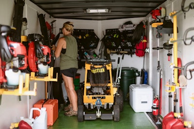 Female landscaper putting away tools inside a landscaping trailer