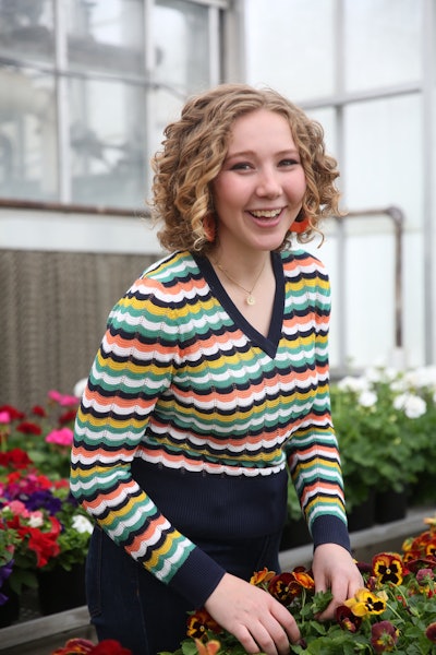 Renata Goossen, winner of the John Deere scholarship, stands with pansy flowers in greenhouse