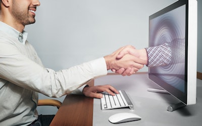 man sitting in front of desktop shaking hands with arm coming through the desktop screen