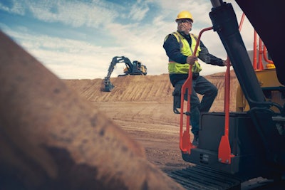 man with hardhat stands on volvo construction equipment at jobsite