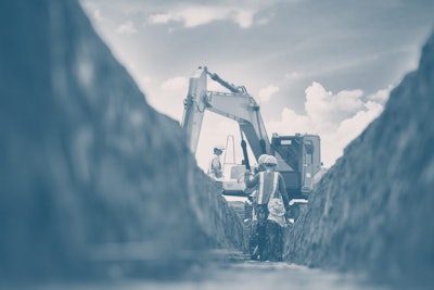 construction workers in a shallow trench with an excavator at a job site