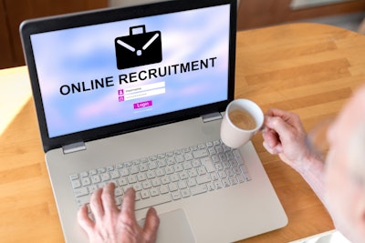 a person drinking coffee while logging in to an online recruitment page on a laptop