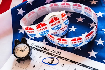 November 2020 calendar with election day circled, clock, and roll of 'i voted' stickers on an american flag