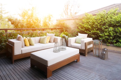 Outdoor patio couch, chair, table, and decorations on a deck, surrounded by landscaping plants