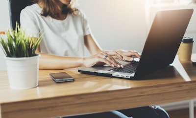 woman sits at desk with laptop, phone, coffee, and desk plant