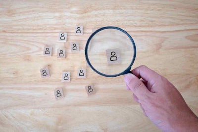 A hand focusing a magnifying glass over a wooden tile representing a person