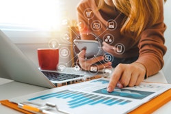 Social and technology icons stemming from a phone while a person points at graphs beside an open laptop