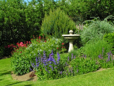 A berm wall built up with flowering plants and a bird bath in the center