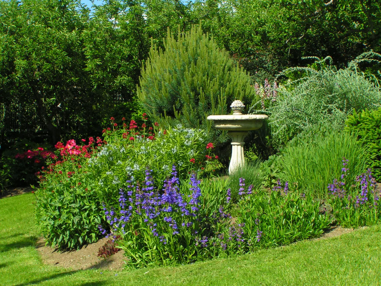 A berm wall built up with flowering plants and a bird bath in the center