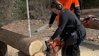 Beth Presley using a chainsaw to cut a log into slices