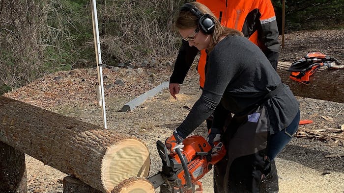 Beth Presley using a chainsaw to cut a log into slices