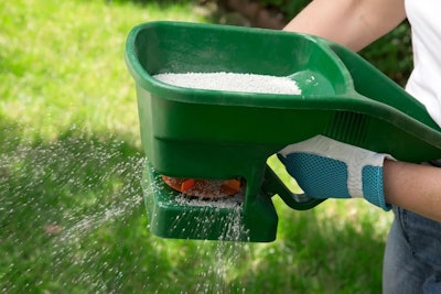 landscaper spreads fertilizer with a handheld garden spreader