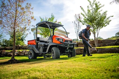 Kubota’s gas-powered RTV520 utility vehicle next to a landscaper clearing leaves with a backpack blower