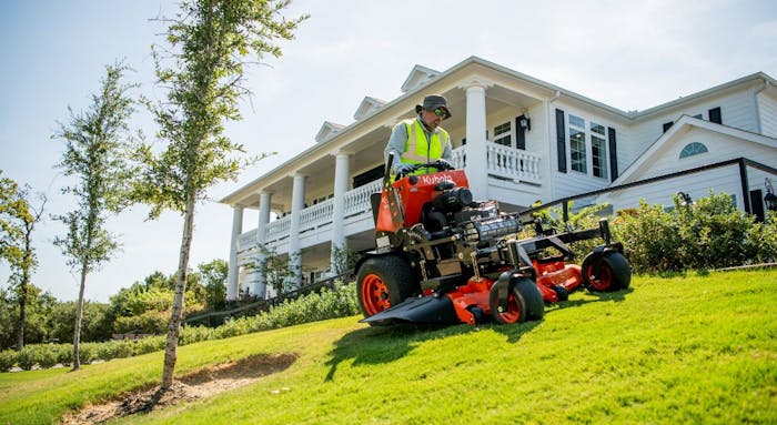 A landscaper cutting grass with a Kubota SZ Series commercial stand-on mower