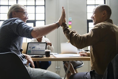 Two workers at a desk high fiving each other