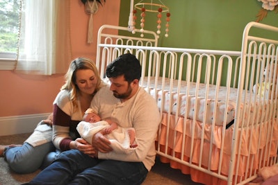 Taylor Sounders and her husband holding their newborn daughter while sitting on the floor of the nursery
