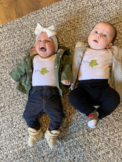 Taylor Sounders’ daughter Seneca (left) and another baby wearing Pickel Landscape Group onesies while laying on the floor
