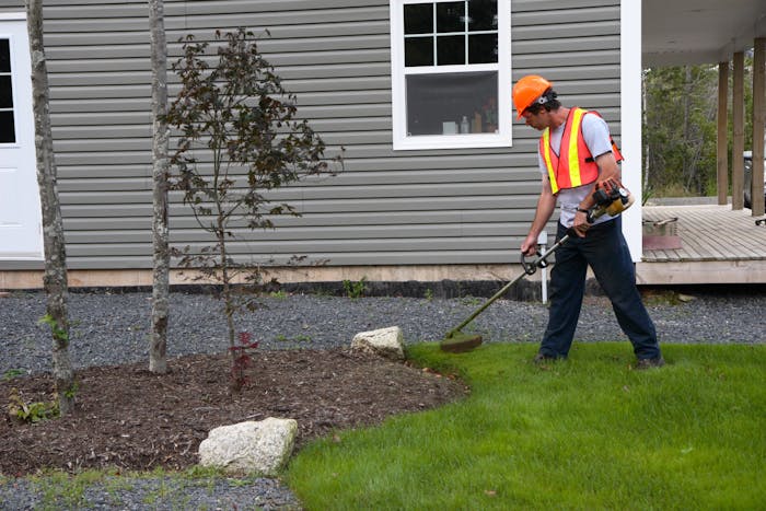 landscaper wearing orange safety vest and hat while edging a yard