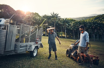 two landscapers standing near a mower and landscaping truck