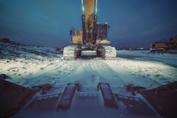 Excavator at snowy construction site at dusk.