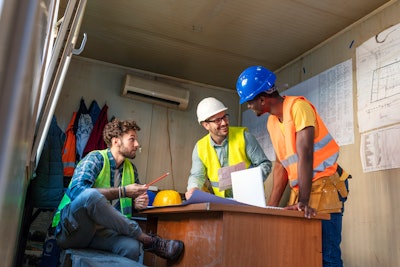 Three workers wearing safety vests inside a job site office trailer