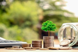 Tree growing out of a stack of coins next to a jar with coins spilled out on a table