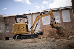Cat 304 compact excavator digging in dirt beside building under construction