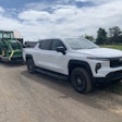 white 2024 Chevy Silverado EV Work Truck hauling John Deere tractor
