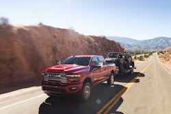red 2025 Ram HD 2500 towing ATVs on mountain highway